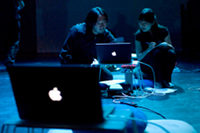 two people look intently into a laptop on stage